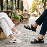 カフェテラスで向かい合って座る2人の足元。白いサンダルと黒いスポーツサンダルを合わせた夏の街歩きコーデ