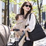 東京の街中で、抱っこ紐で赤ちゃんを抱きながらベビーカーを押して散歩する母親